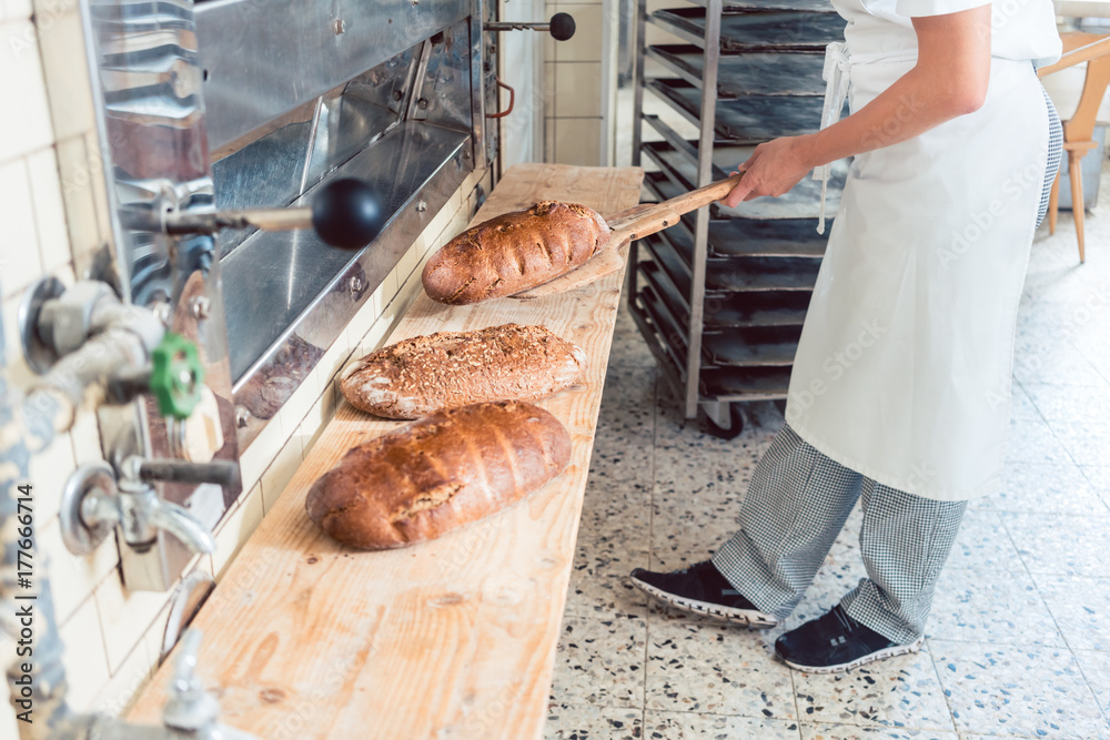 Bäcker Frau in Backstube legt Brot auf Brett ab Bäcker Frau in Backstube legt Brot auf Brett ab