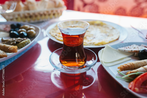 A cup of hot fragrant black tea. Two plates with vegetarian food - fresh vegetables and cheese, cake and drink in glass on red table