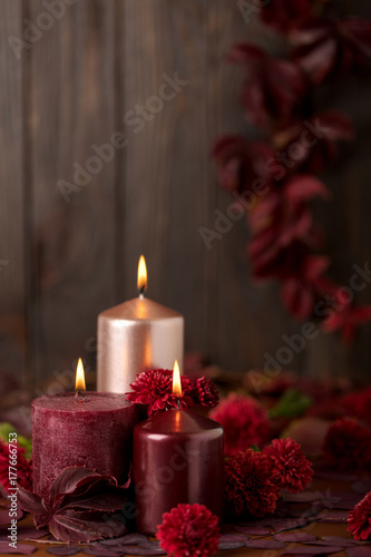 Three candles of crimson and pink color on a dark background with cones, leaves and daisies.