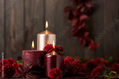 Three candles of crimson and pink color on a dark background with cones, leaves and daisies.