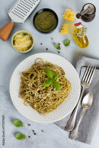 Pasta spaghetti with pesto sauce, basil and parmesan cheese on a white ceramic plate and gray concrete or stone background. Traditional Italian dish. Selective focus. Top view.