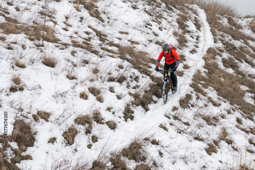 Cyclist in Red Riding Mountain Bike on the Snowy Trail. Extreme Winter Sport and Enduro Biking Concept.