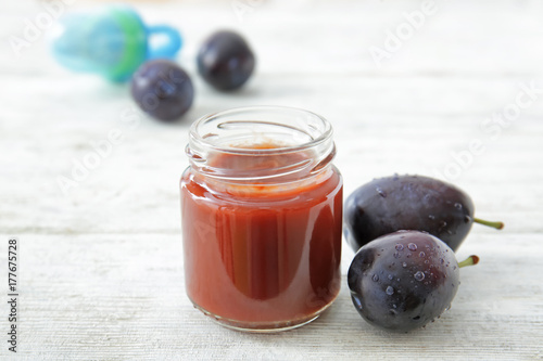 Jar with baby food and plums on table