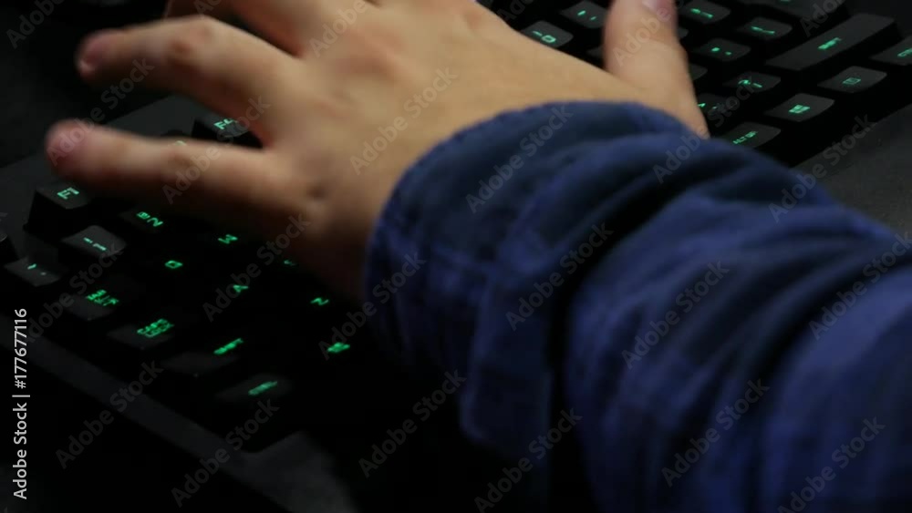 Man hands typing on a gaming computer keyboard. Keyboard with green-blue light. Neon light. Man hands typing on a gaming computer keyboard. Keyboard with green-blue light. Neon light.