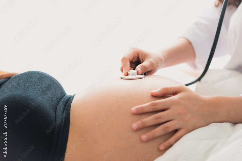 Obstetrician doctor use stethoscope to listen the heartbeat through the  pregnant mother's stomach Stock Photo | Adobe Stock