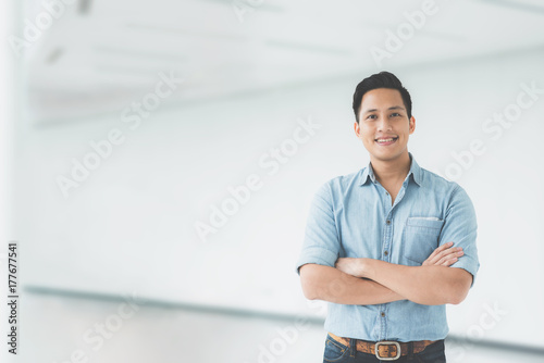Confident Asian man smiling with arm crossed in modern office building