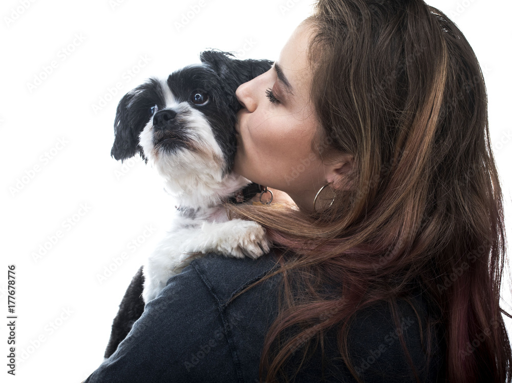 Portrait of a beautiful young woman kissing her Lhasa Apso dog in a photography studio against a white background with the dog looking towards the light Portrait of a beautiful young woman kissing her Lhasa Apso dog in a photography studio against a white background with the dog looking towards the light