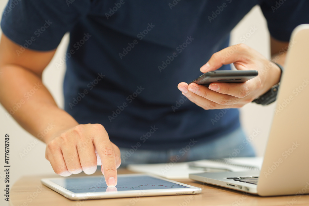 Fototapeta premium close up trader man hand swipe on tablet with stock graph dashboard and holding smartphone for check news at desk , multitasking people concept