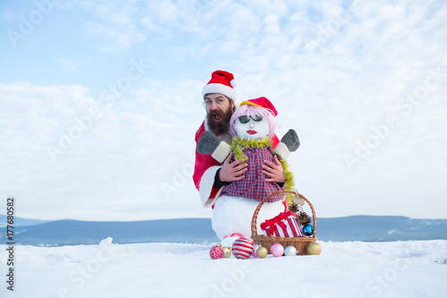 Man in santa hat hugging snowman