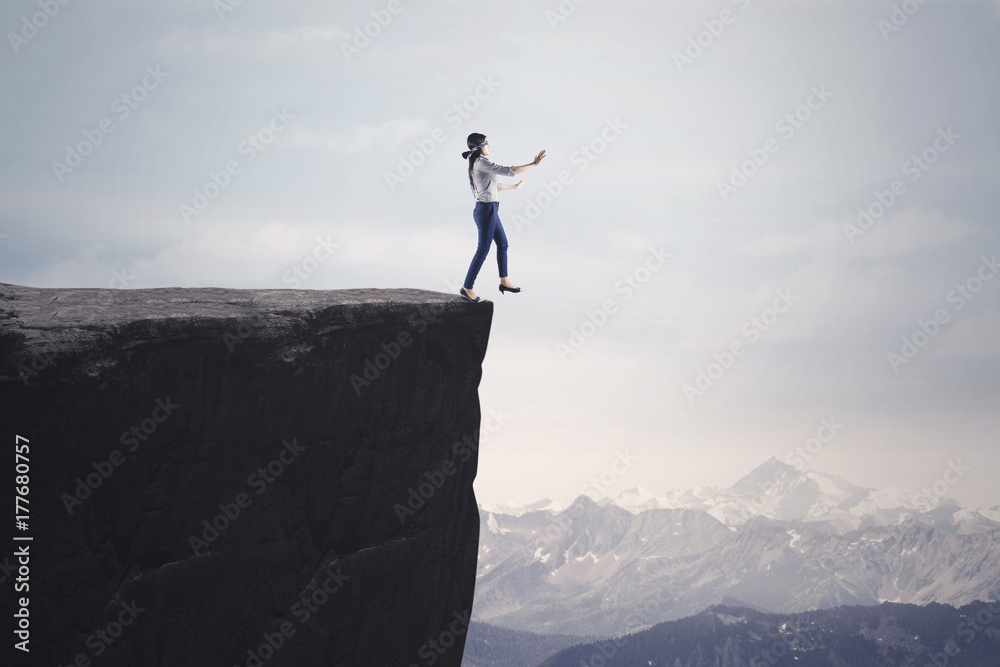 Blindfolded businesswoman walks toward cliff Blindfolded businesswoman walks toward cliff