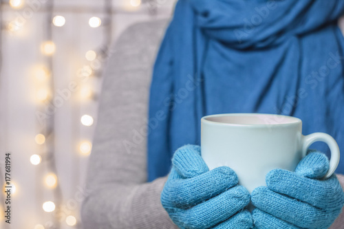 A cup of hot tea, a drink in mittens. Christmas concept. New Year's decor. Garlands and scarf.