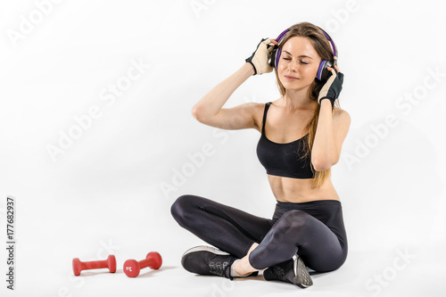 Dark hair girl, wearing a black top and leggins, is listening to music in headphones in the white isolated background