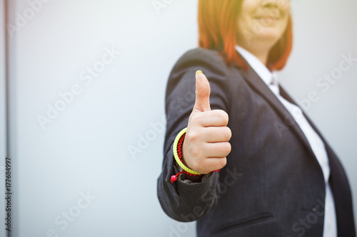 Success! Victory! Happy successful red-haired girl boss, businesswoman in suit shows gesture class, with space for text and advertising photo