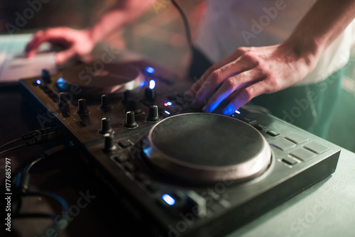 Hands of man DJ tweak various track controls on dj's deck at night club 