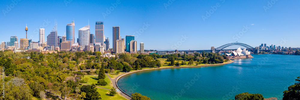 Fototapeta premium Piękna panorama dzielnicy portowej w Sydney z mostem Harbour Bridge, ogrodem botanicznym i budynkiem Opery.