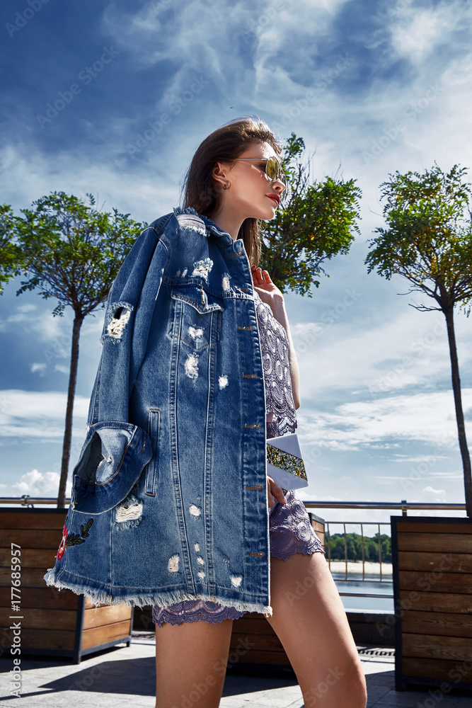 Street style look woman sexy wear denim jeans jacket brunette hair walk square sunglasses accessory trees summer time fashion glamor beautiful date designer clothes. Stock Photo | Adobe