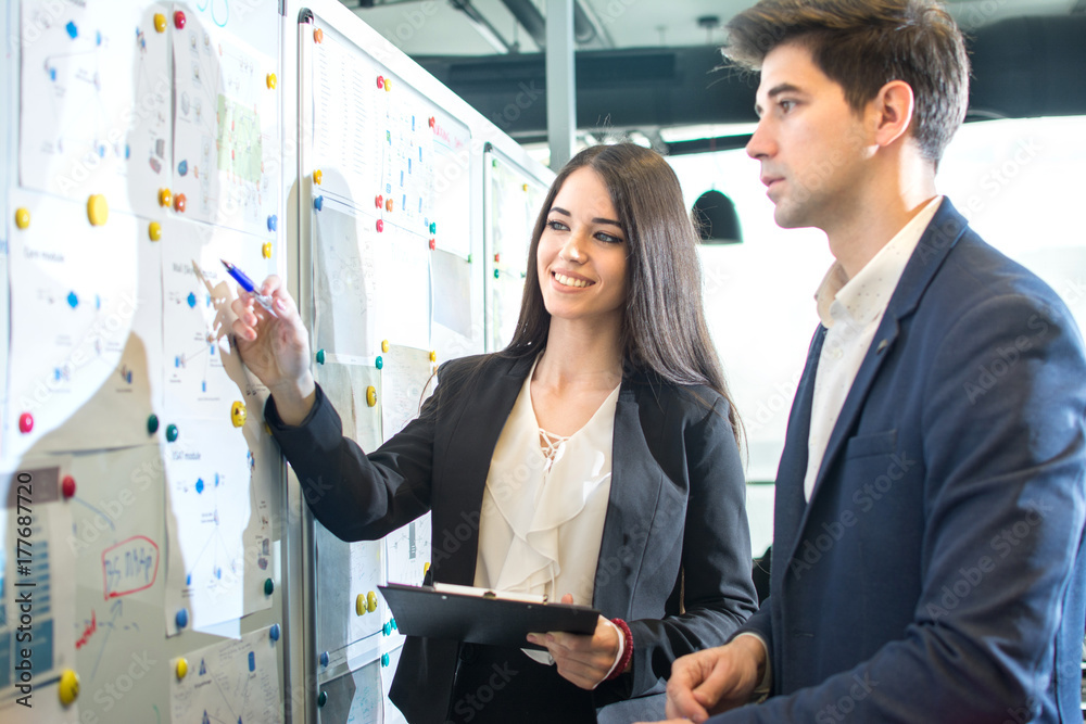 Φωτογραφία Young smiling businesswoman presenting business strategy on board to her male colleague in the board room