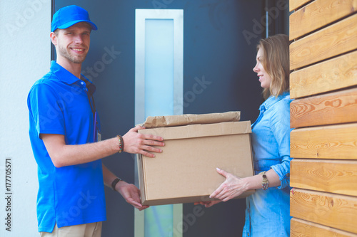 Smiling delivery man in blue uniform delivering parcel box to recipient - courier service concept. Smiling delivery man in blue uniform © lenets_tan