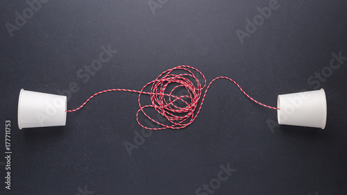 Two white paper cup connect with red rope used for classic phone on black stone table board. For old communication system concept