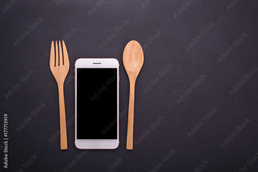 Smartphone, spoon and fork on black stone table background, concept Eating technology Smartphone, spoon and fork on black stone table background, concept Eating technology