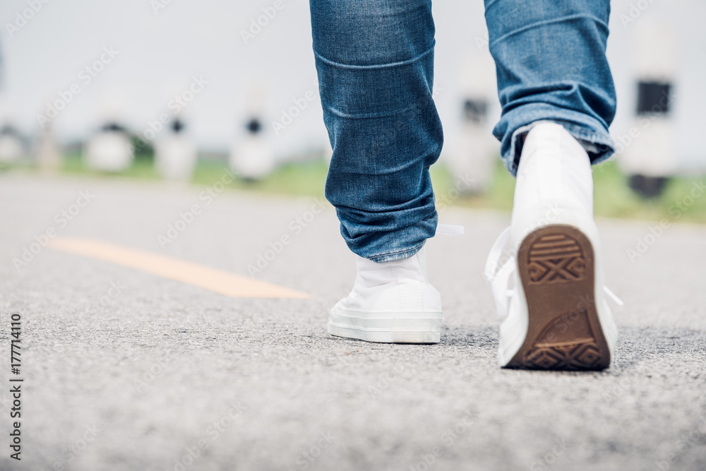 Close up woman wear jean and white sneaker walking forward on highway road in sunny day,Alone travel or solo traveler concept