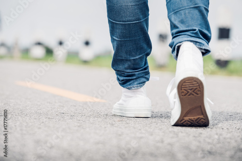 Close up woman wear jean and white sneaker walking forward on highway road in sunny day Alone travel or solo traveler concept