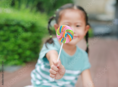 Little asian girl giving swirl lollipop candy for you.