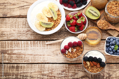 Tasty granola with berries in glasses and bowl on wooden table