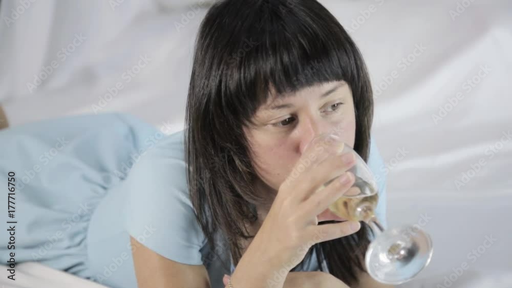 lonely young attractive woman lies on a bed in a bedroom, drinks champagne lonely young attractive woman lies on a bed in a bedroom, drinks champagne