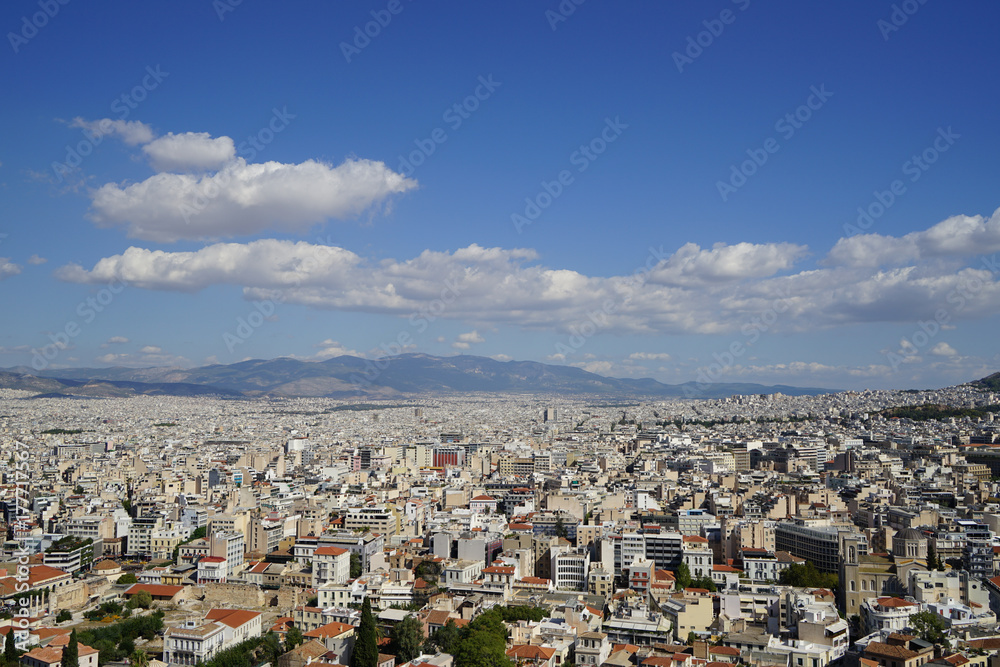 View of Athens cityscape showing lowrise white buildings architecture, mountain, trees, white cloud and blue sky background