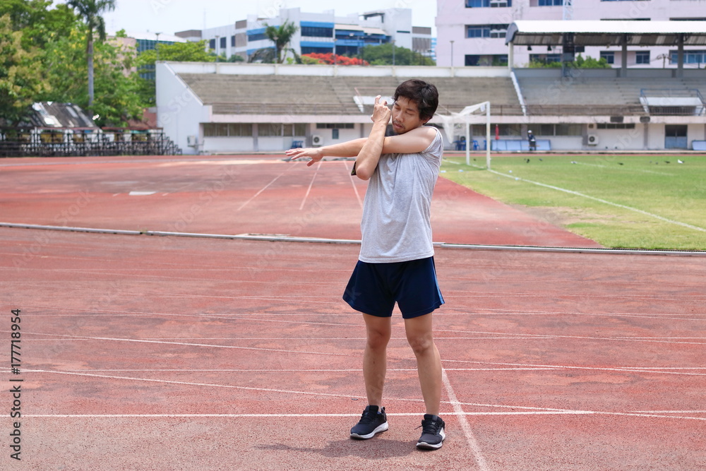 Healthy young Asian runner man warming up before run on track in the stadium