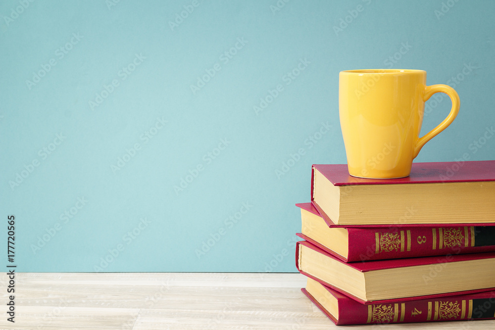 Stack of books and yellow mug against blue background. Copy space for text. Stack of books and yellow mug against blue background. Copy space for text.
