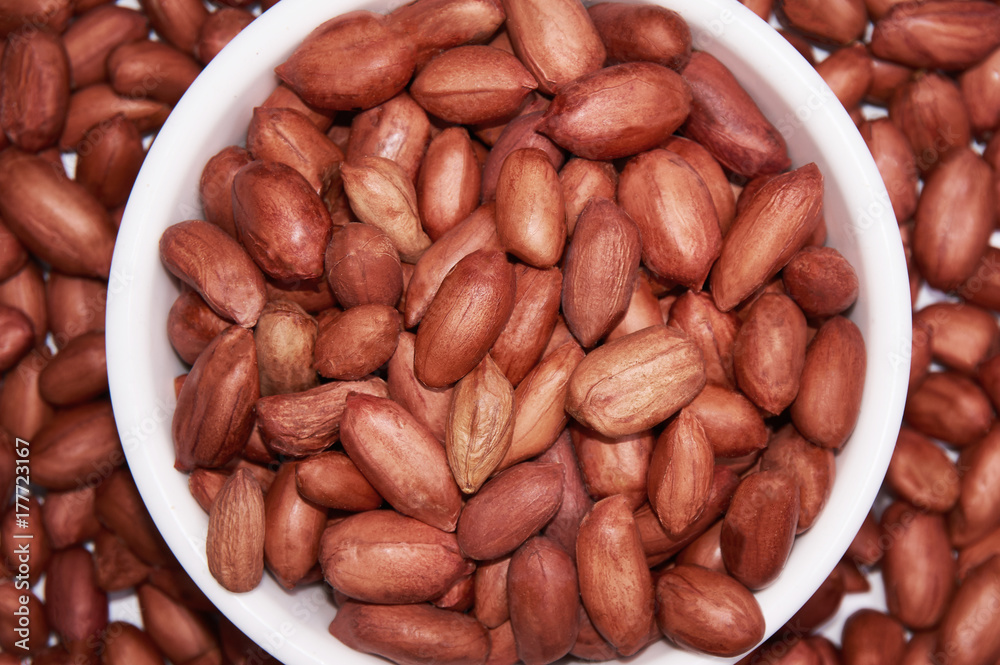 Peanuts in a white bowl on a background of peanuts. Food background. Peanuts in a white bowl on a background of peanuts. Food background.