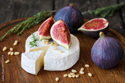 Camembert cheese with fresh purple figs, thyme and pine nuts on cutting board