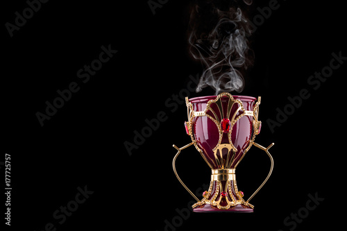 Red And Gold Arabic Traditional Incense Bukhoor Agar Wood Burner In A Mabkhara With Smoke Isolated On Black Background. Used In Majlis, Ramadan And Eid Occasions. Blank Text Space