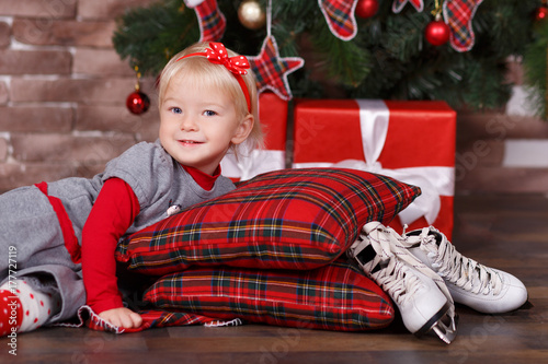 Christmas beautiful cute baby girl posing in casual clothes close to new year pine green tree with presents pillows and toy horse in studio scene