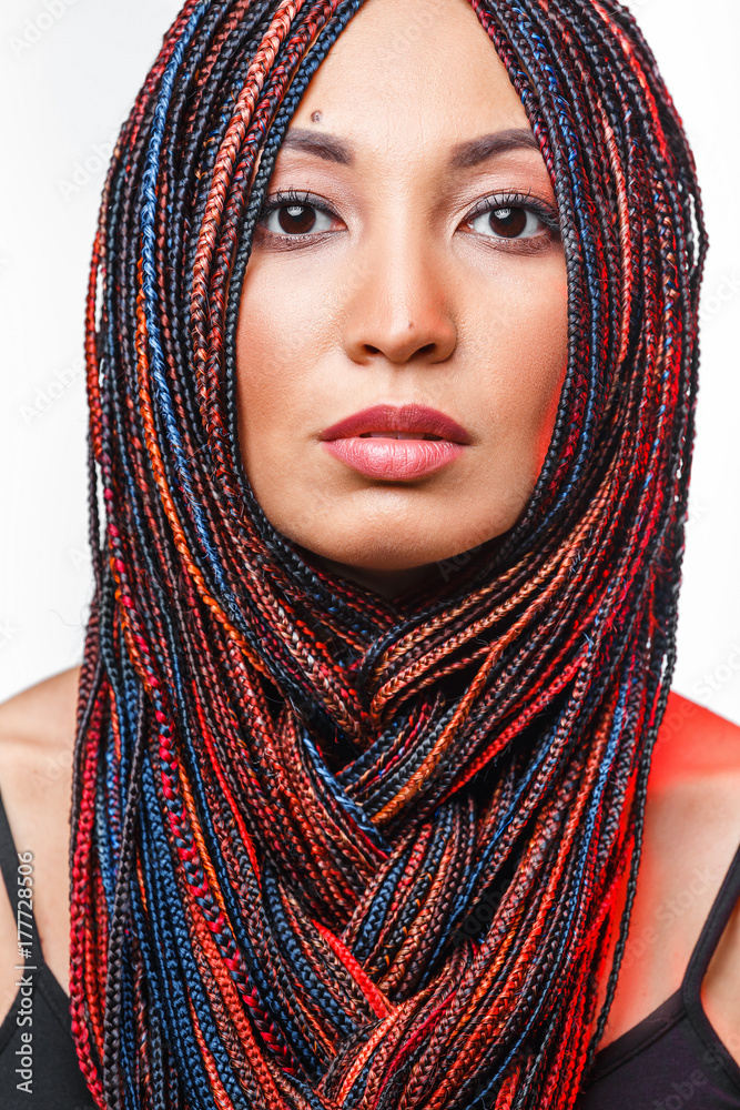 Fashion studio shoot of a mixed race woman with a creative colorful hairstyle in the form of a pigtail braided from dreadlocks in the technique of zizi. The concept of hairdressing art