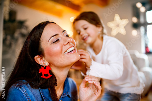 Young mother with daughter decorating Christmas tree together.