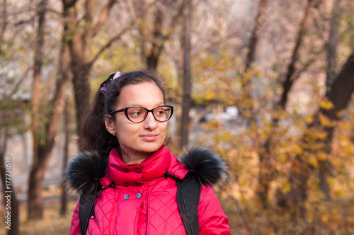 Beautiful girl in a red jacket with a backpack stands in the autumn forest © Beliakina Ekaterina
