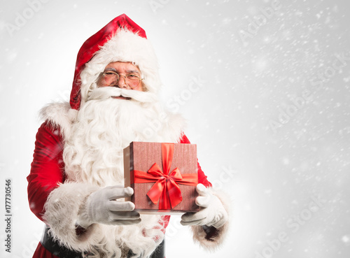 Santa Claus holding a bag with presents over a white/gray background 