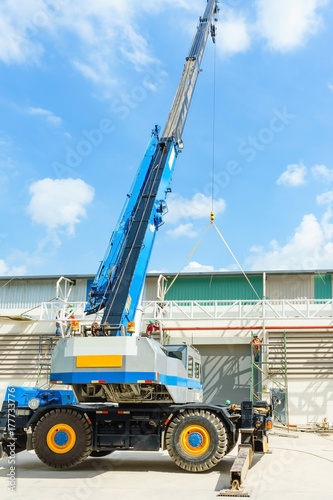 blue hydraulic truck crane standing on a construction site under construction. A worker is standing on a scissor lift at a suitable height to help positioning it.