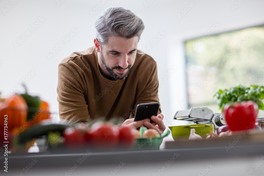 Man using a smartphone while standing in the kitchen Man using a smartphone while standing in the kitchen