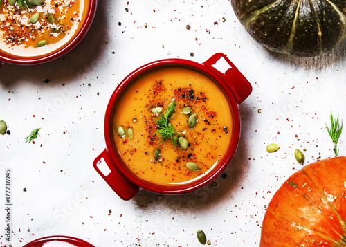 Spicy pumpkin soup in red pan, white background, top view