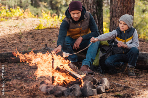 father and son cooking marshmallows in forest