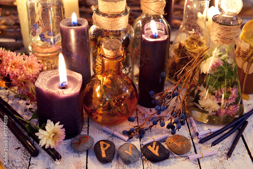 Magic runes, black candles, flowers and berries on witch table in candle light