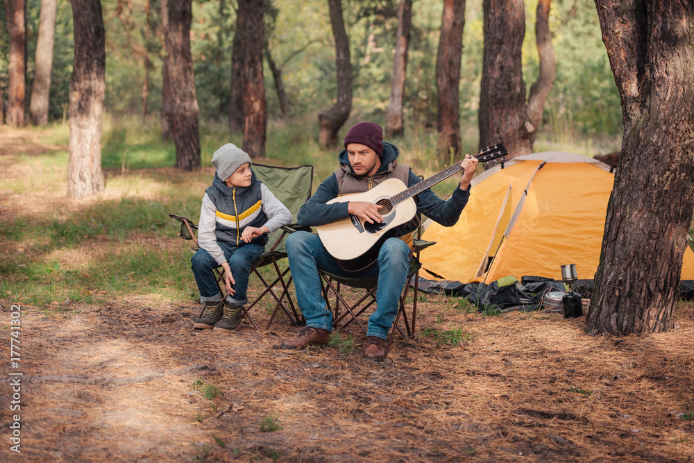 father and son with guitar in forest father and son with guitar in forest