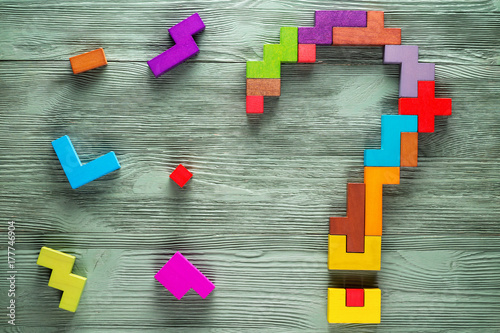 Question mark made of colorful wooden blocks on green wooden background, top view. Concept of creative, logical thinking.