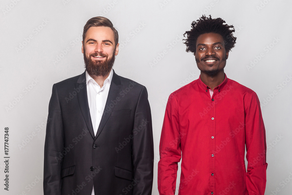 Two partners to business, standing near each other, looking at camera and toothy smiling Two partners to business, standing near each other, looking at camera and toothy smiling