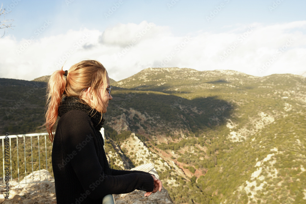 Naklejka premium A middle-aged woman, dyed hair, a sweater and a scarf, stands on a viewing platform in the mountains