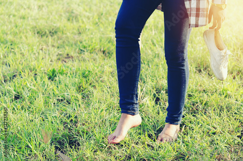 Young woman Holding white sneakers walking on tet green grass barefoot in the garden alone in the morning Soft sunlight